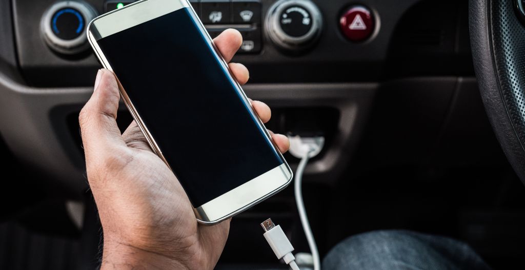 Man driving car with phone charging in hand